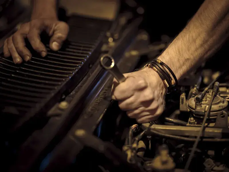 Hands with grease working on a car engine with a metal wrench